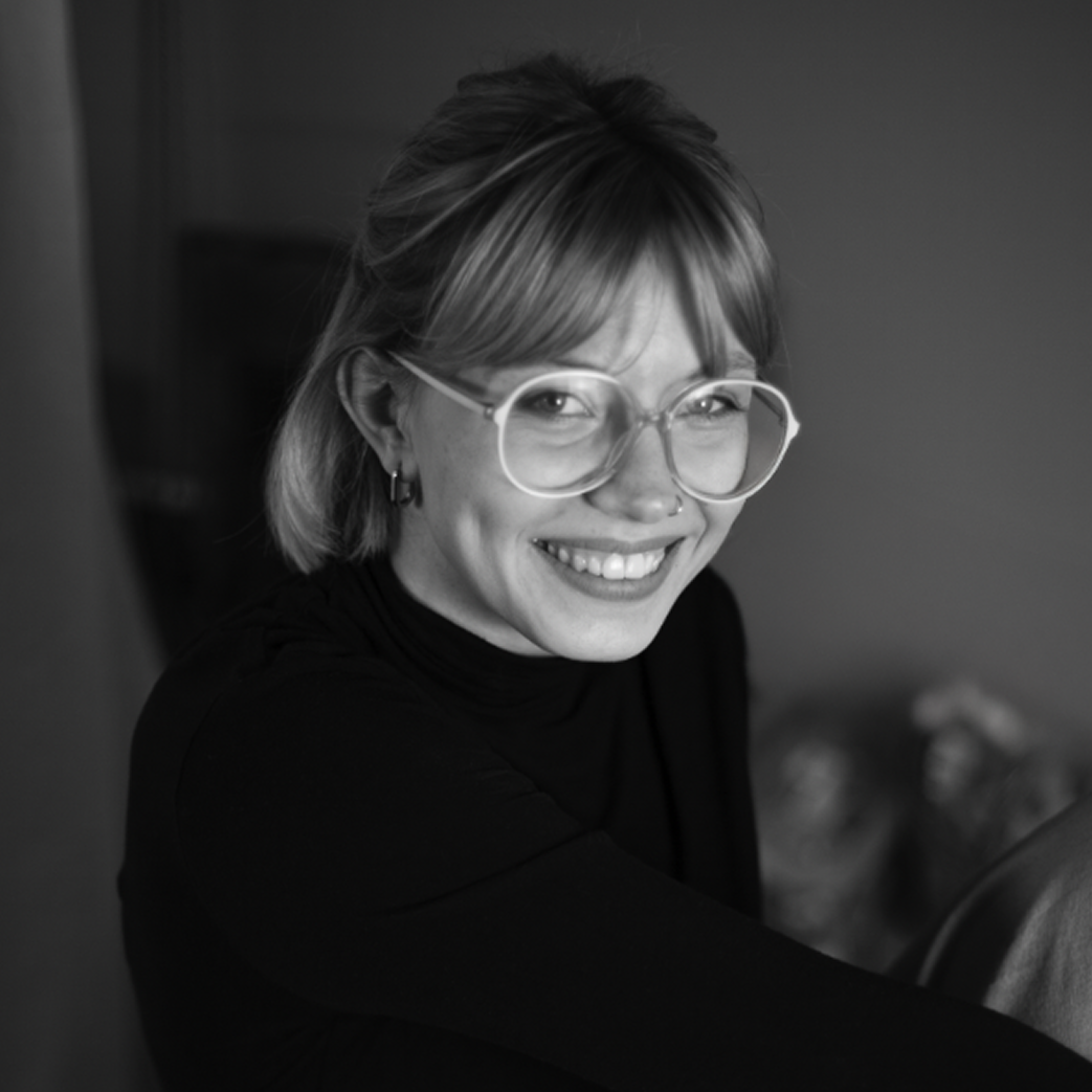 Portrait of a man with brown hair and glasses on a flat gray background.
